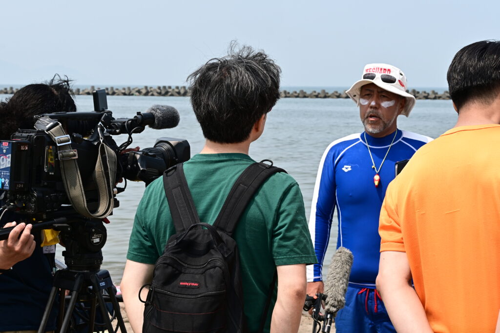 海岸でテレビの取材を受けるライフセーバー