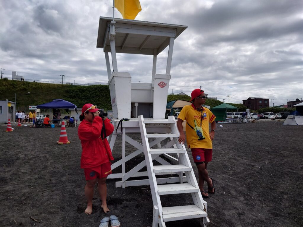 厚田海浜プールの監視台で、双眼鏡で水面を監視するライフセーバーと無線を持つライフセーバー