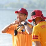 海水浴場で、無線を身につけて仲間と笑顔で話すライフセーバー