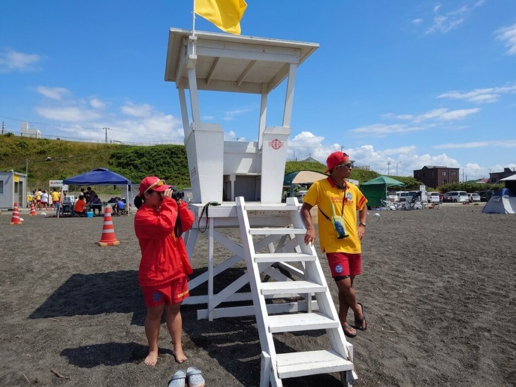 厚田海浜プールの監視台で、双眼鏡で水面を監視するライフセーバーと無線を持つライフセーバー